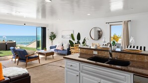A modern kitchen with a large island, a dining area with a view of the ocean, and a living room with a sofa and chairs. - Single Family Gorgeous Beachfront Mansion on the Sand P1733-0 (Oceanside)