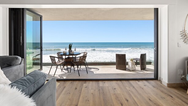 A modern living room with a large glass door leading to a beach view. - Single Family Gorgeous Beachfront Mansion on the Sand P1733-0 (Oceanside)