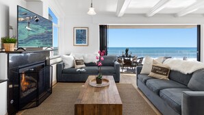 A modern living room with a large TV, comfortable seating, a fireplace, and a view of the ocean. - Single Family Gorgeous Beachfront Mansion on the Sand P1733-0 (Oceanside)