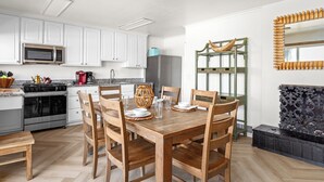 Een moderne keuken met witte kastjes, een magnetron, een fornuis en een eethoek met houten stoelen en een tafel.