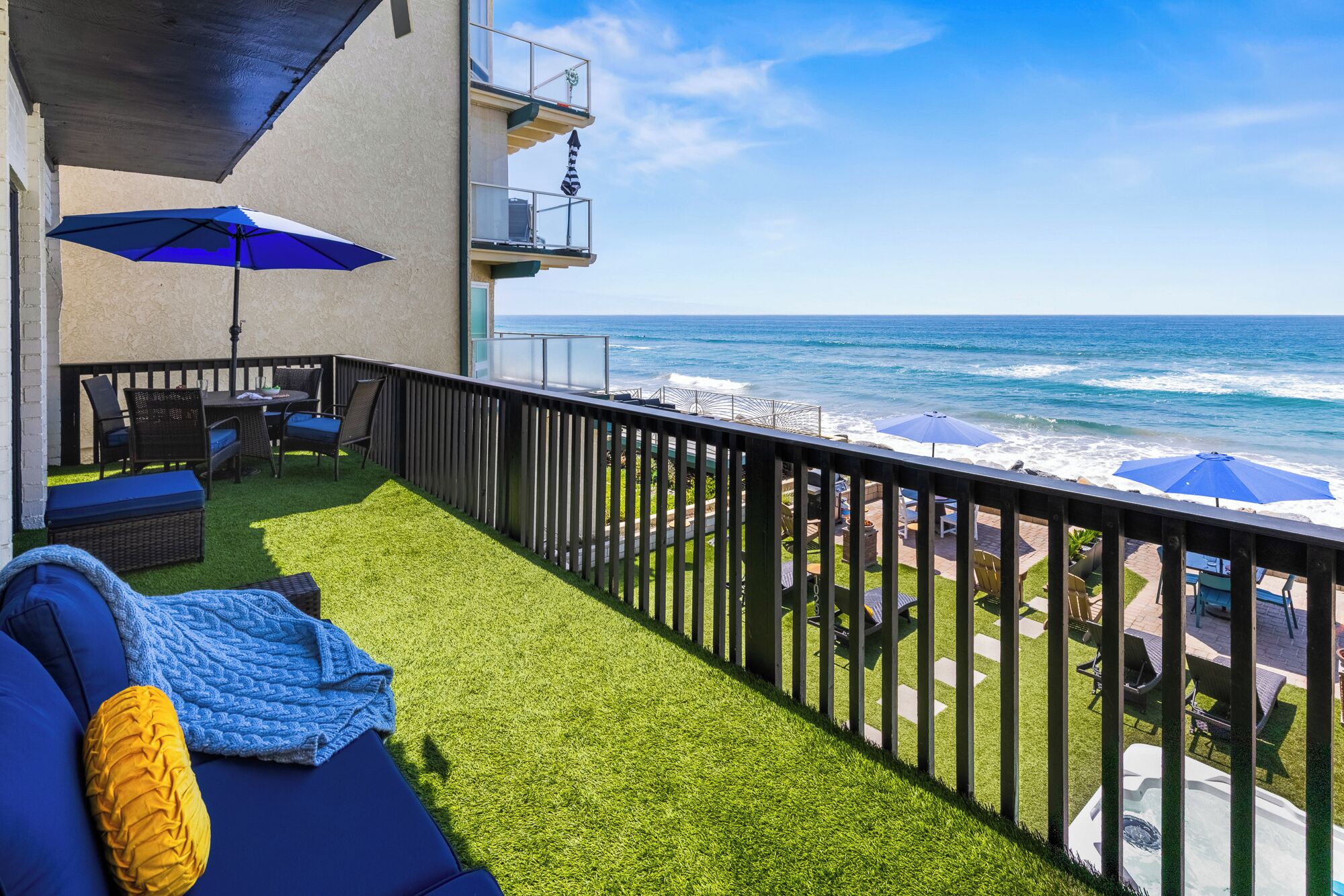 A balcony with a view of the ocean, a small seating area with a table and chairs, and a grassy area.