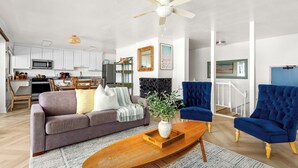 Een moderne woonkamer met een bank, twee fauteuils, een salontafel en een eethoek, met een keuken op de achtergrond.