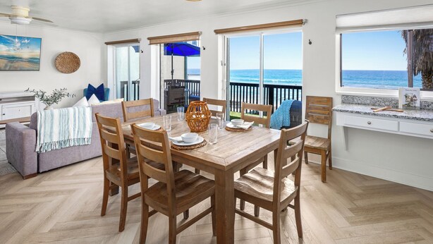 Een eethoek met een houten tafel en stoelen, een uitzicht op de oceaan door grote ramen, en een balkon met uitzicht op zee.