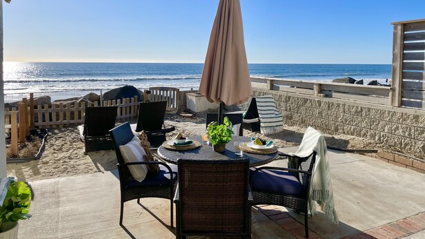 A patio with wicker furniture, a table with a plate of food, and a view of the ocean. - Oceanfront Getaway with Private Sandy Beach - 1615-1 (Oceanside)
