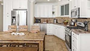 A modern kitchen with white cabinetry, a wooden dining table, and a stone backsplash. - Single Family Beautiful Home with Two Spas P815-X (Oceanside)