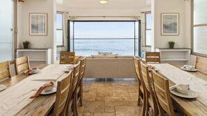 A dining area with a view of the sea, featuring wooden furniture, a ceiling fan, and framed artwork. - Luxurious Single Family Pet Friendly Oceanfront Home with Two Spas P825-X (Oceanside)