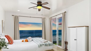 Une chambre avec un lit, un ventilateur de plafond, une vue sur l’océan et une porte-fenêtre coulissante.