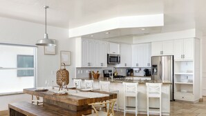 Une cuisine moderne avec des meubles blancs, une table à manger en bois et une grande fenêtre.