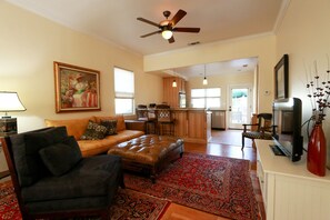 A living room with a sofa, ottoman, and a red patterned rug. There is a ceiling fan, a television, and a painting on the wall. - Olive with a Twist-Right in the Heart of Paso Robles on the West Side! (Paso Robles)