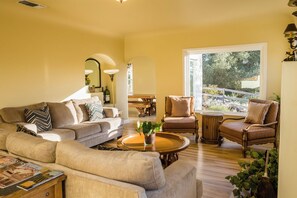 A living room with a sofa, armchairs, a coffee table, and a dining table.