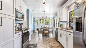 A modern kitchen with white cabinets, stainless steel appliances, and a dining area with a table and chairs. - Coconut Beach House: 4BR Pool Home in Clearwater (Clearwater Beach)
