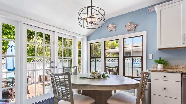 A kitchen with a round table, chairs, a hanging light fixture, and a view through large windows. - Coconut Beach House: 4BR Pool Home in Clearwater (Clearwater Beach)