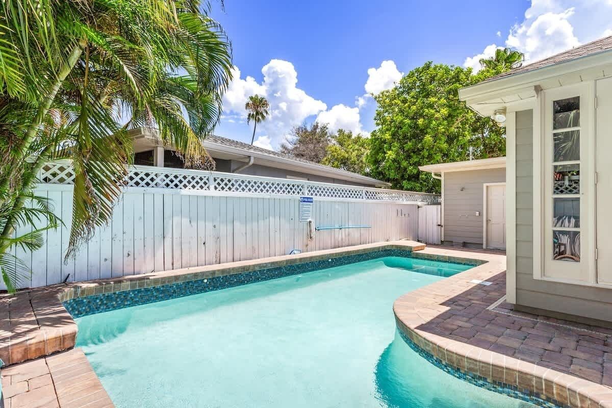 A swimming pool with a wooden deck, a white fence, and a small building with glass doors.