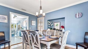 A dining area with a wooden table, white chairs, and a chandelier. - Coconut Beach House: 4BR Pool Home in Clearwater (Clearwater Beach)