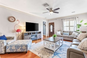 A living room with a flat-screen TV, a ceiling fan, a sofa, a coffee table, and a patterned rug.