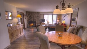 Un comedor con una mesa y sillas de madera, una chimenea de piedra y un televisor al fondo.