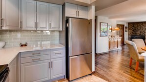 Una cocina moderna con armarios grises, un refrigerador de acero inoxidable y una chimenea de piedra al fondo.