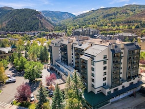 A multi-story hotel with a central courtyard, surrounded by trees and a mountainous backdrop. - Large Condo w Mtn Views A704 (Avon)