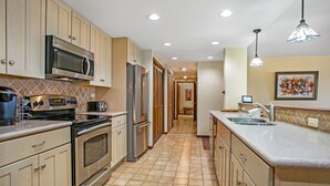 Une cuisine avec des meubles de couleur beige, des appareils électroménagers en acier inoxydable, un carrelage au sol et des luminaires suspendus.