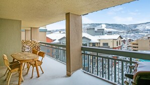 Un balcon avec une table et des chaises en bois, donnant sur un paysage enneigé où l’on aperçoit des bâtiments au loin.