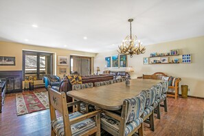 A spacious dining area with a large wooden table and patterned upholstered chairs, a chandelier, and a fireplace.