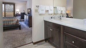 Habitación de hotel con cama, escritorio, cómoda, espejo grande y baño con lavabo y toallero.