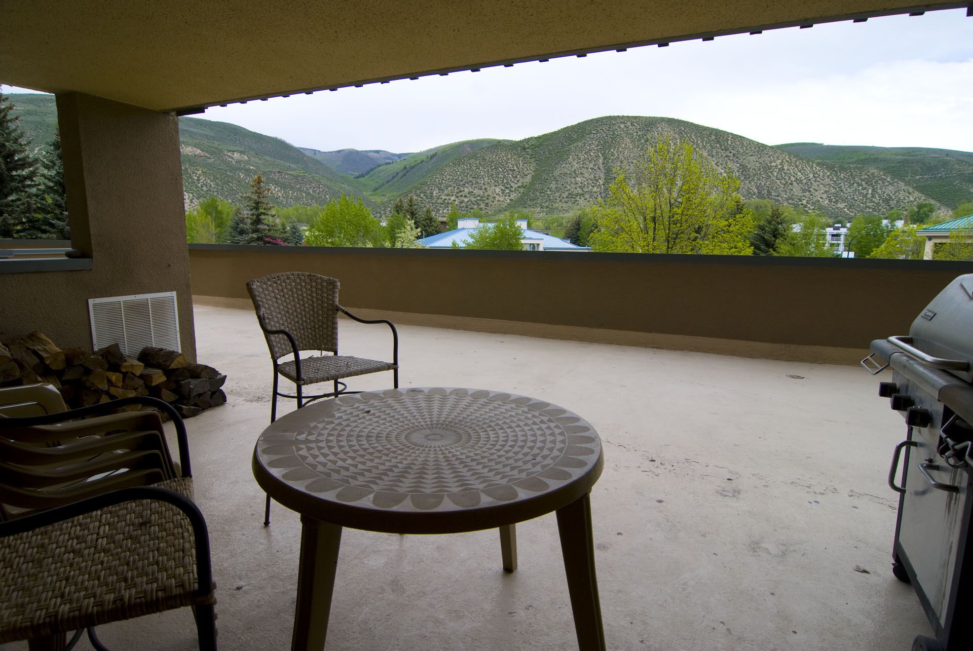 A balcony with a table and chairs, a grill, and a view of mountains.
