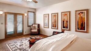 A bedroom with a bed, a chair, a ceiling fan, and four framed pictures on the wall. - Vineyard Views + Jetted Tub | Paso Robles Wine Country | Solitude I (Paso Robles)