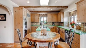 A kitchen with wooden cabinets, a central island, and a dining table with chairs. - Vineyard Views + Jetted Tub | Paso Robles Wine Country | Solitude I (Paso Robles)