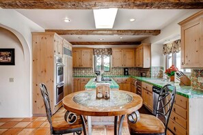 A kitchen with wooden cabinets, a central island, and a dining table with chairs. - Vineyard Views + Jetted Tub | Paso Robles Wine Country | Solitude I (Paso Robles)