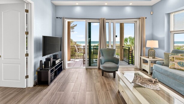 A living room with a TV, seating, a balcony with a view, and a door. - Treasure Island Villa, Beachfront, Private Pool! (Treasure Island)