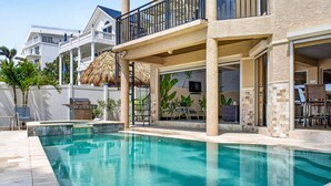 A swimming pool with a thatched roof, outdoor seating, and a view of a multi-story building. - Treasure Island Villa, Beachfront, Private Pool! (Treasure Island)