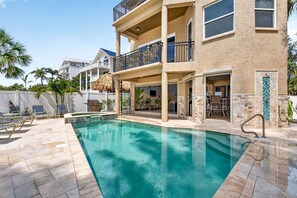 A swimming pool with a two-story building, outdoor seating, and palm trees.
