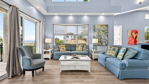A spacious living room with a blue sofa set, a white coffee table, and a large window offering a view of the outdoors. - Treasure Island Villa, Beachfront, Private Pool! (Treasure Island)