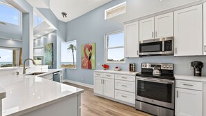 A modern kitchen with white cabinets, a stainless steel oven, a microwave, and a large window. - Treasure Island Villa, Beachfront, Private Pool! (Treasure Island)