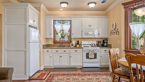 A kitchen with white cabinets, a stove, a microwave, and a dining area with a wooden table and chairs. - 2 Ensuite Suites + Walk to Downtown | Paso Robles | Lewis Loft (Paso Robles)