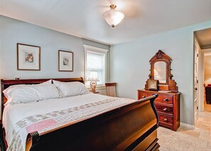 A bedroom with a bed, a dresser, a mirror, and two framed pictures on the wall.