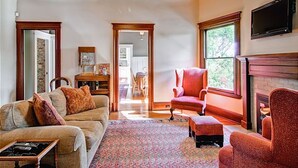 A living room with a sofa, armchair, and ottoman, a fireplace, and a television mounted on the wall.