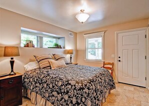 A bedroom with a bed, bedside lamps, a window, and a door.