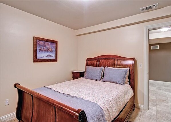A bedroom with a wooden bed, a nightstand, a painting on the wall, and a door leading to another room.