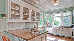 A kitchen with white cabinetry, a large island with a sink, and a view of the outdoors through the windows. - Spa + Chef's Kitchen | Downtown Paso Robles | Downtown Diggs (Paso Robles)
