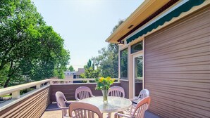 An outdoor patio with a round table and chairs, a vase with flowers, and a view of trees and buildings.
