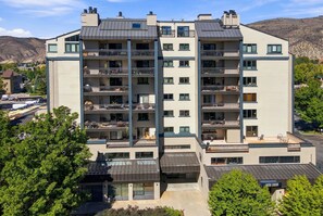 A multi-story residential building with balconies, a flat roof, and a parking area in the foreground.