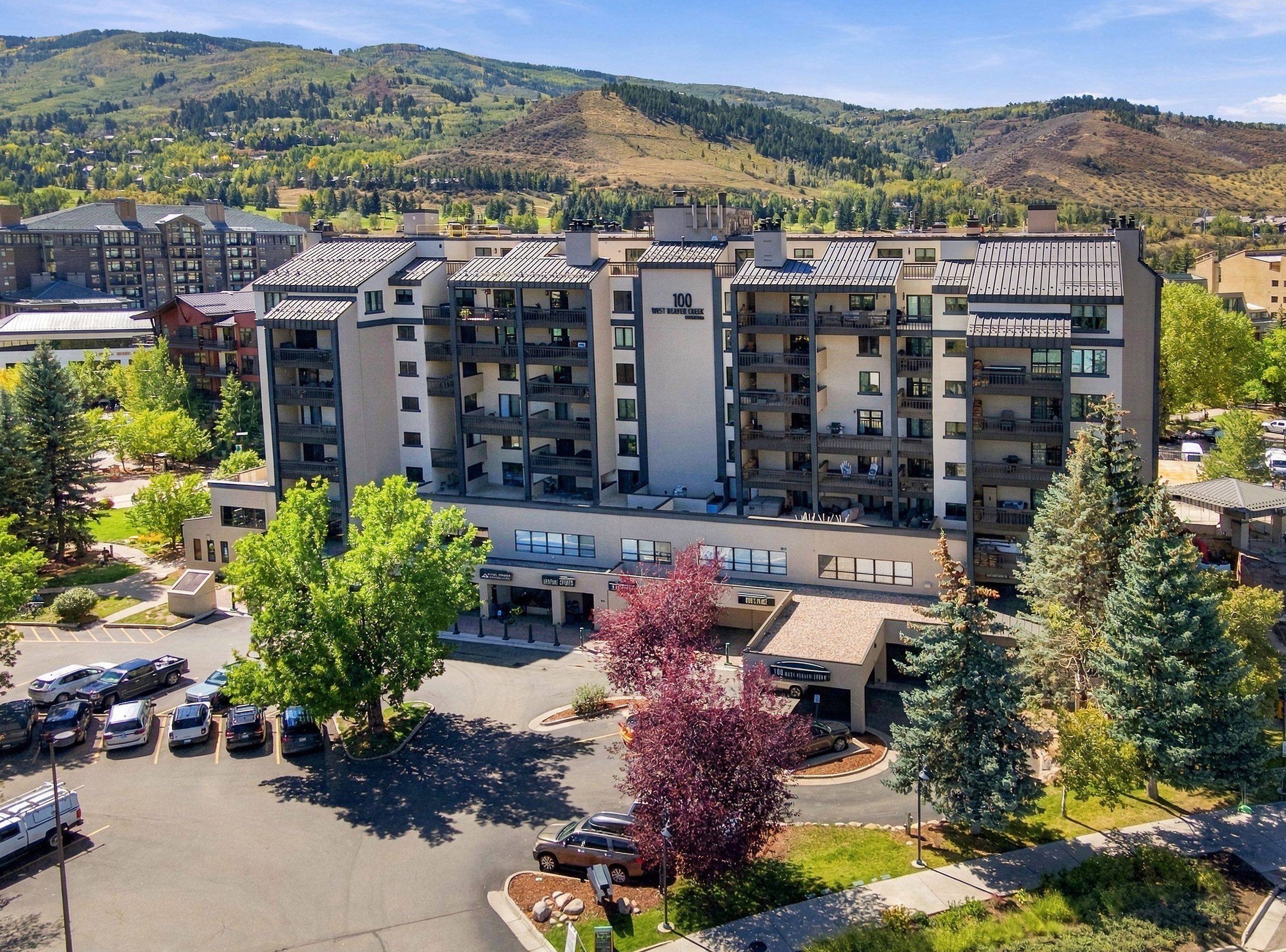 A multi-story hotel with balconies, a parking lot, and a mountainous backdrop.