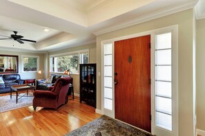 A spacious living room with hardwood flooring, a leather sofa, a red armchair, and a black bookshelf.