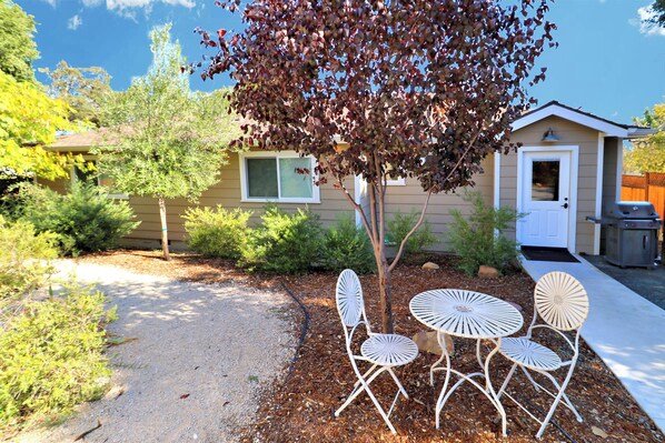 A residential property with a gravel driveway, a small patio with white metal chairs and tables, and a house with a front door and window.