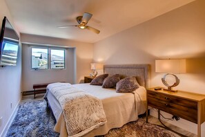 Un dormitorio con cama, mesitas de noche, ventilador de techo y ventana con vistas a las colinas.
