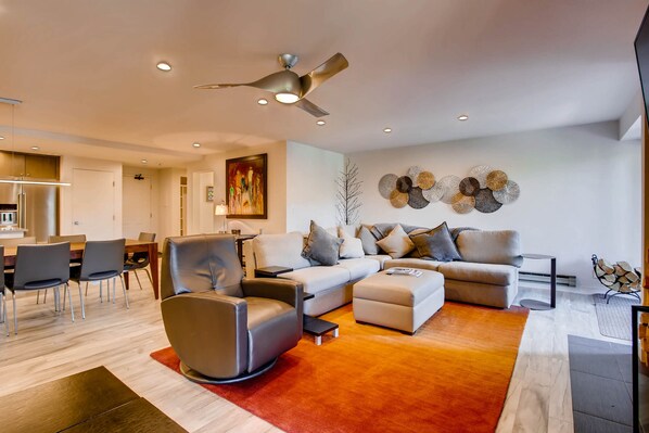 Una sala de estar moderna con sofá, sillones, comedor y ventilador de techo.