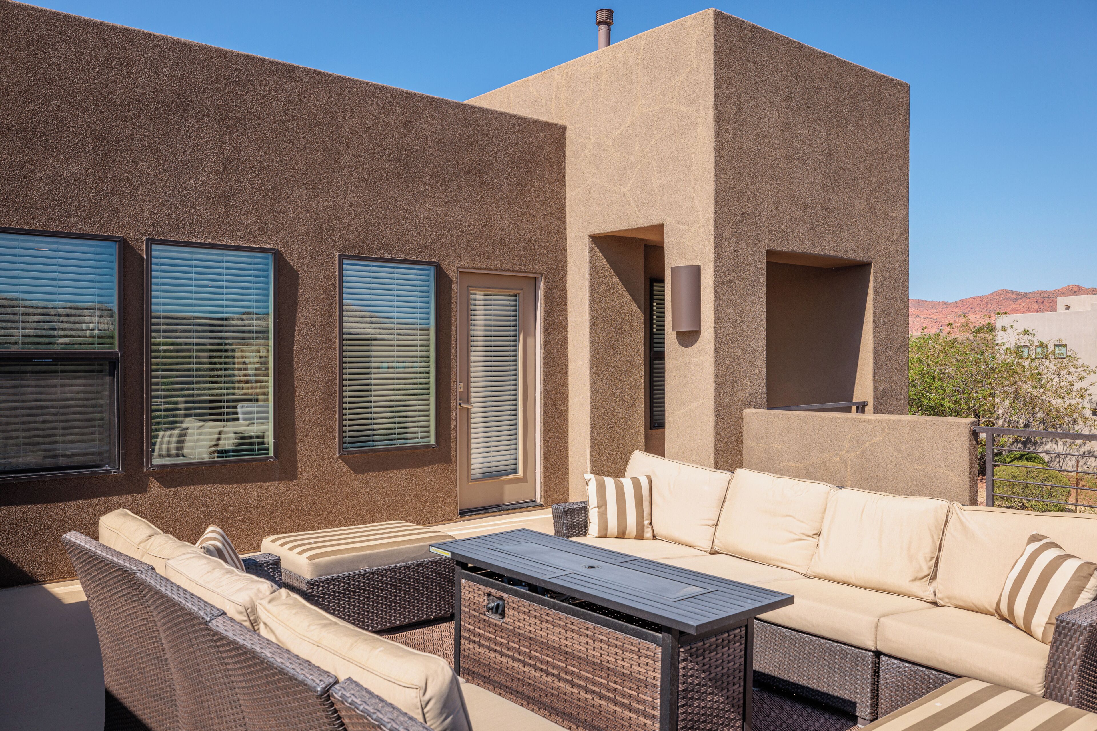 An outdoor seating area with a sofa, a table, and three windows with blinds.