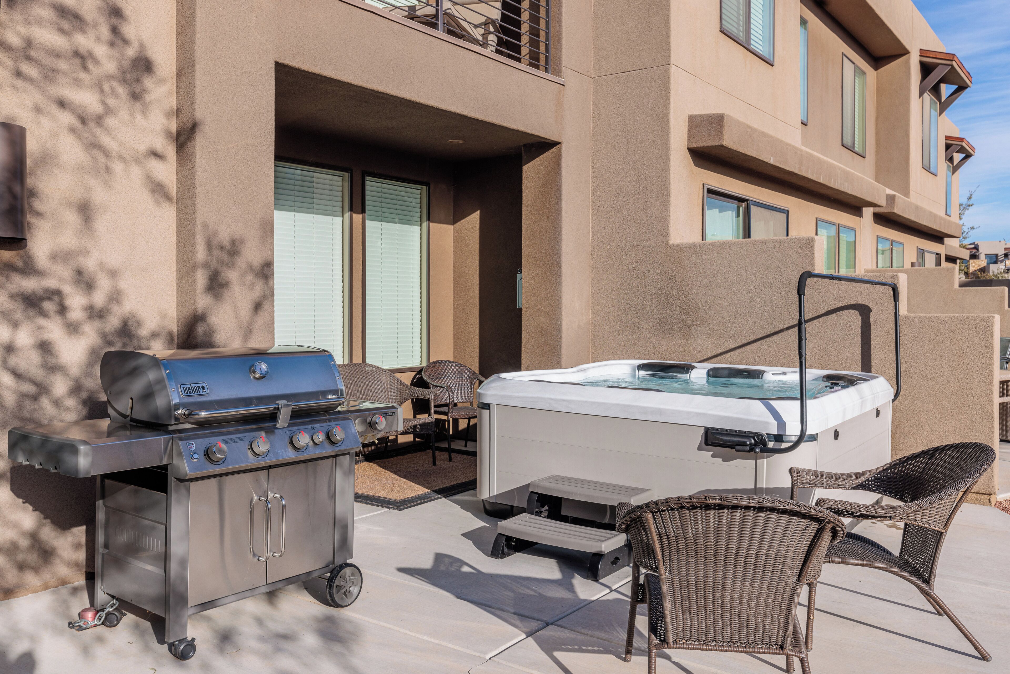 Une terrasse extérieure équipée d’un barbecue, d’un jacuzzi et de fauteuils en osier.